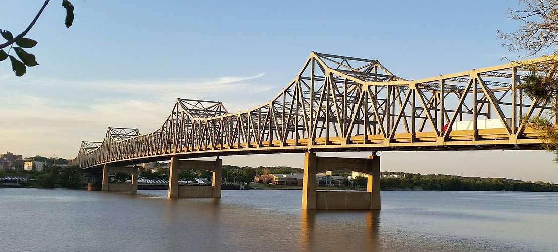 Steel bridge over calm river at sunset.
