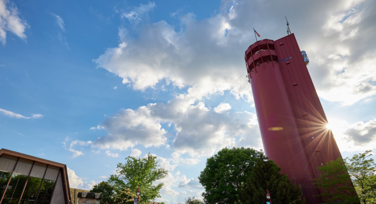 Red water tower against blue sky with clouds.